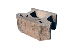 A tan, textured concrete segmental retaining wall block with a hollow core and a tapered shape.