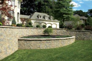 A curved stone retaining wall creates a raised garden bed in a front lawn near a house.