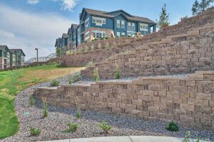 Terraced retaining walls built with brown stone blocks set into a sloped hillside near modern apartment buildings.