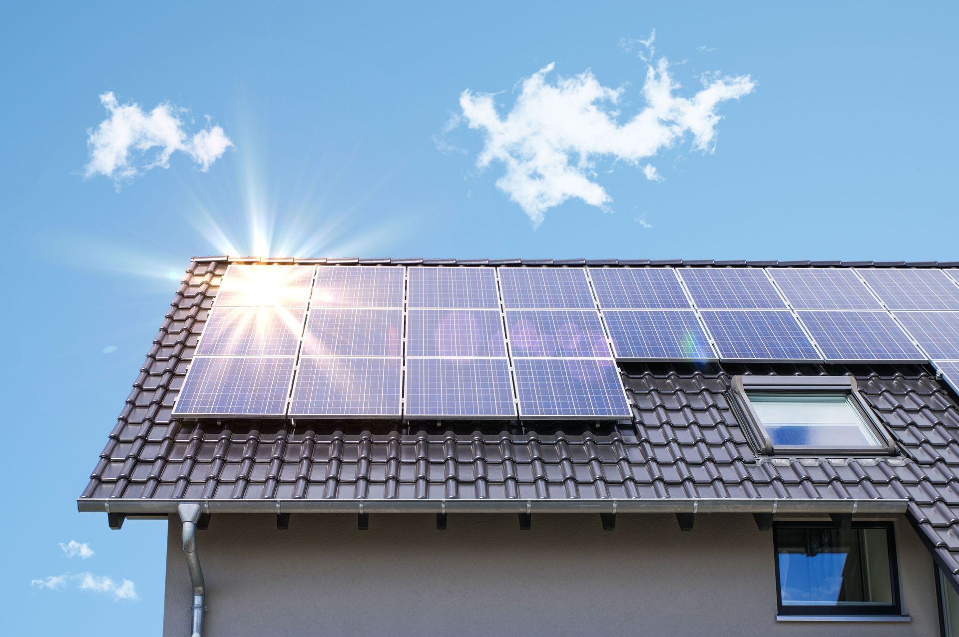 Solar panels on a house roof, catching sunlight, blue sky background.