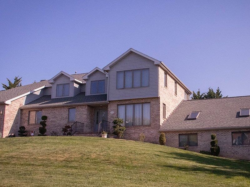 Two-story brick house on a grassy hill, with a blue sky.