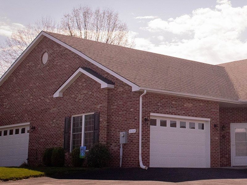 Brick townhome with white garage doors and brown roof.