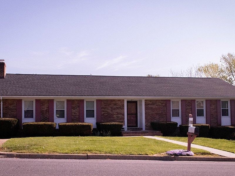 Brick ranch-style house with black roof, white-framed windows, and red shutters. Green lawn and bushes.