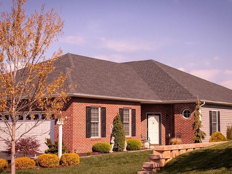 Brick house with dark gray roof, surrounded by a lawn and bushes.