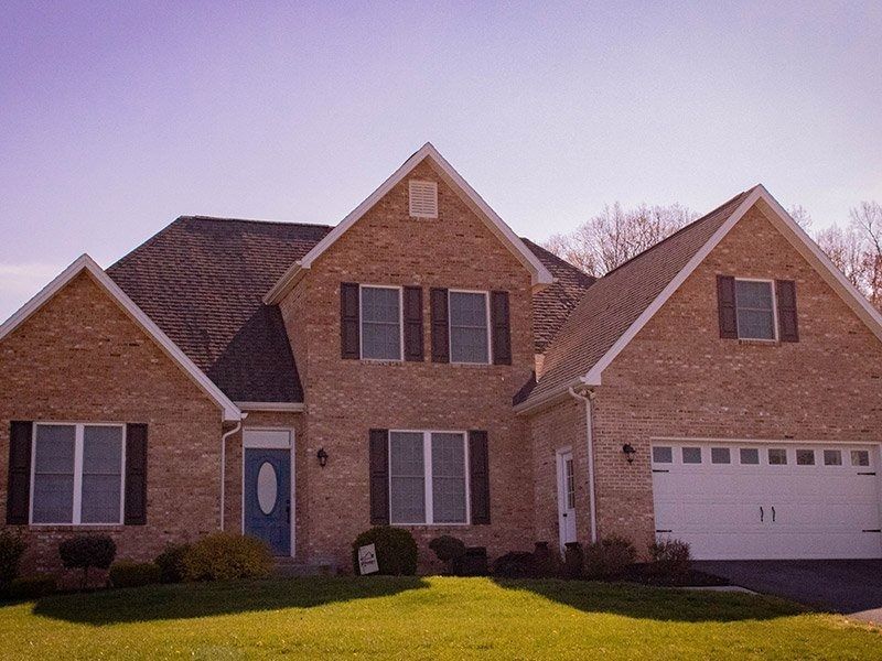 Brick house with a blue door, brown shutters, and a white garage door under a blue sky.