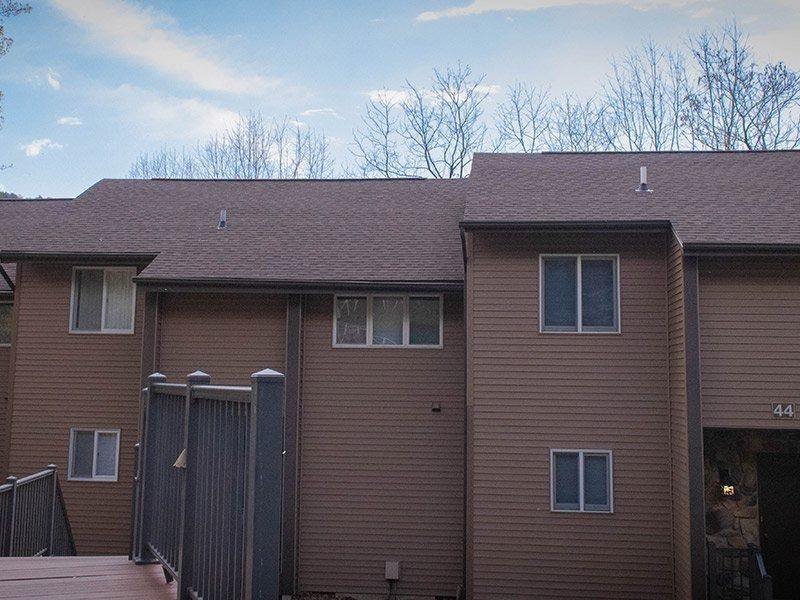 Brown two-story building with multiple windows, brown siding, and a wooden deck. Bare trees and cloudy sky in the background.