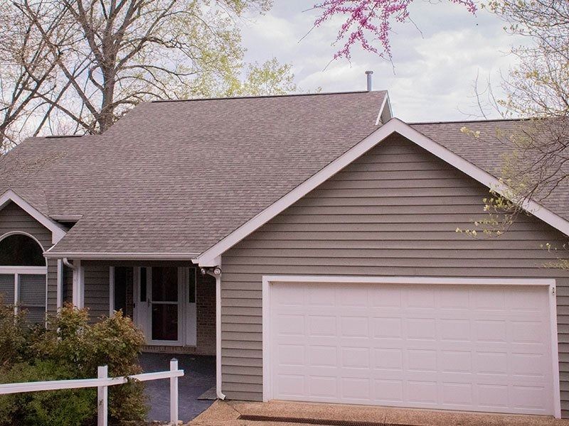 House with gray siding and roof, white garage door, and a flowering tree.