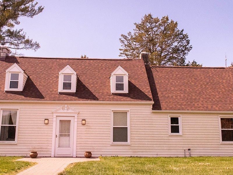 Cream-colored house with a brown roof and three dormer windows. Green grass and a clear sky.