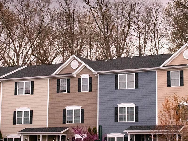 Row of townhouses with varied colored siding and black shutters; leafless trees in the background.