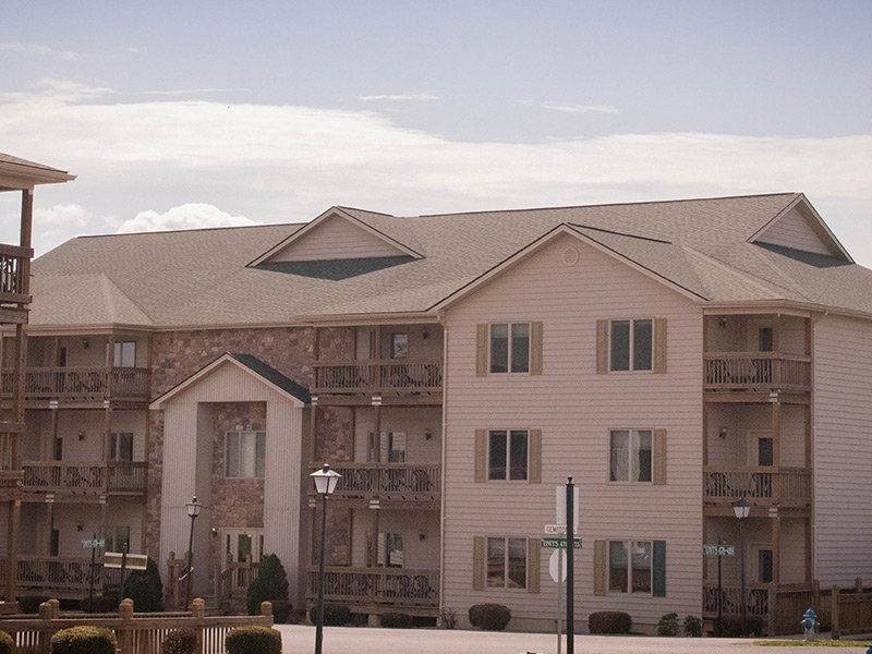 Apartment building with light siding, stone accents, balconies, under a cloudy sky.