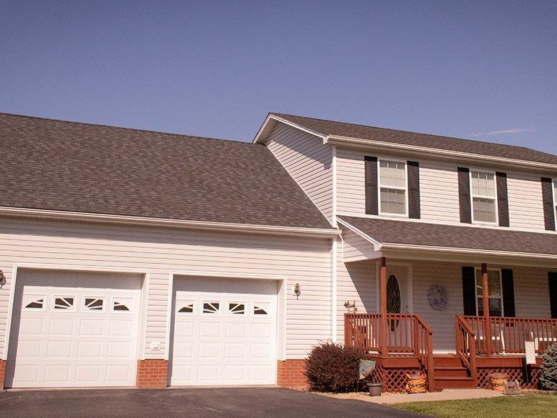 Two-story white house with a two-car garage, brown roof, red brick accents, and a front porch.