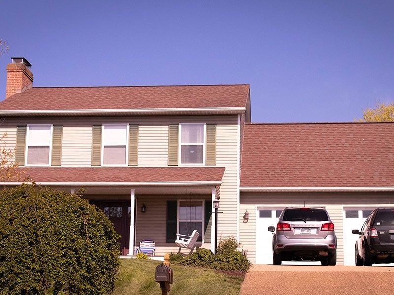 Two-story house with beige siding, brown roof, and two cars parked in the garage.
