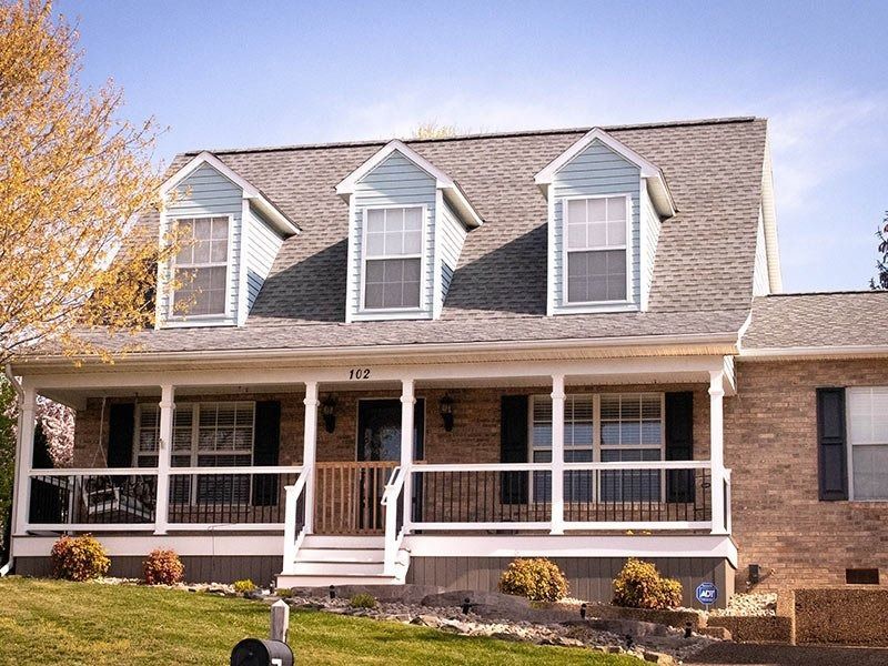 Brick house with a front porch and three dormers. Blue accents, gray roof.