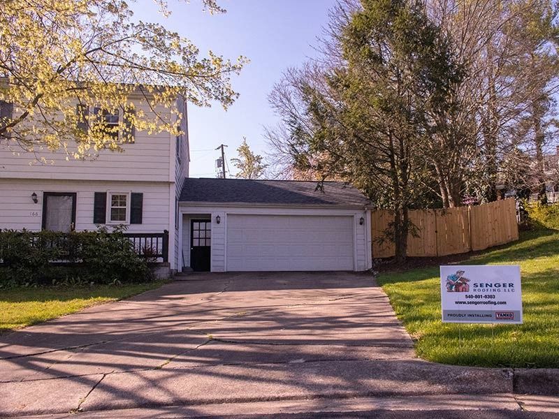 White house with attached garage and long driveway on a sunny day; sign in the yard.
