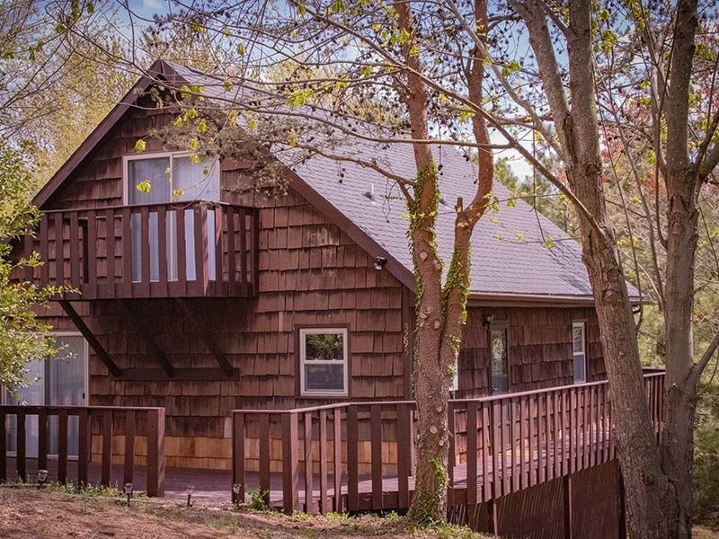 Brown cabin with balcony and deck, surrounded by trees.
