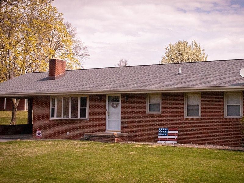 Brick ranch house with a carport, American flag, and a green lawn.