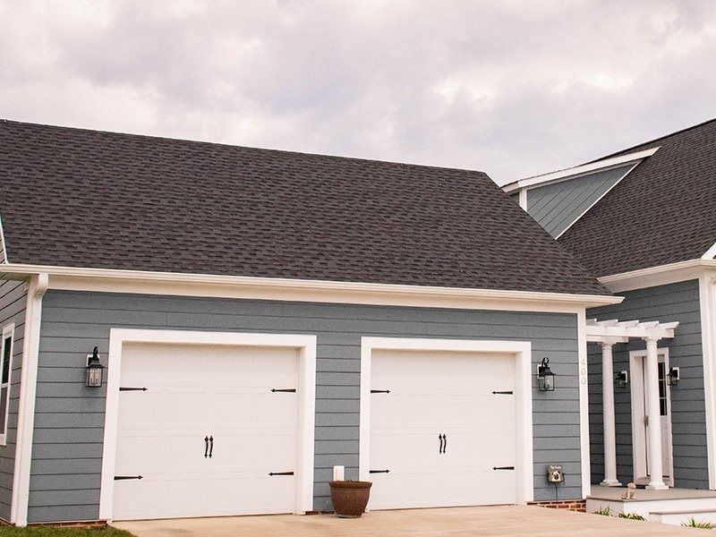 Blue house with white garage doors, black hardware, and gray roof.