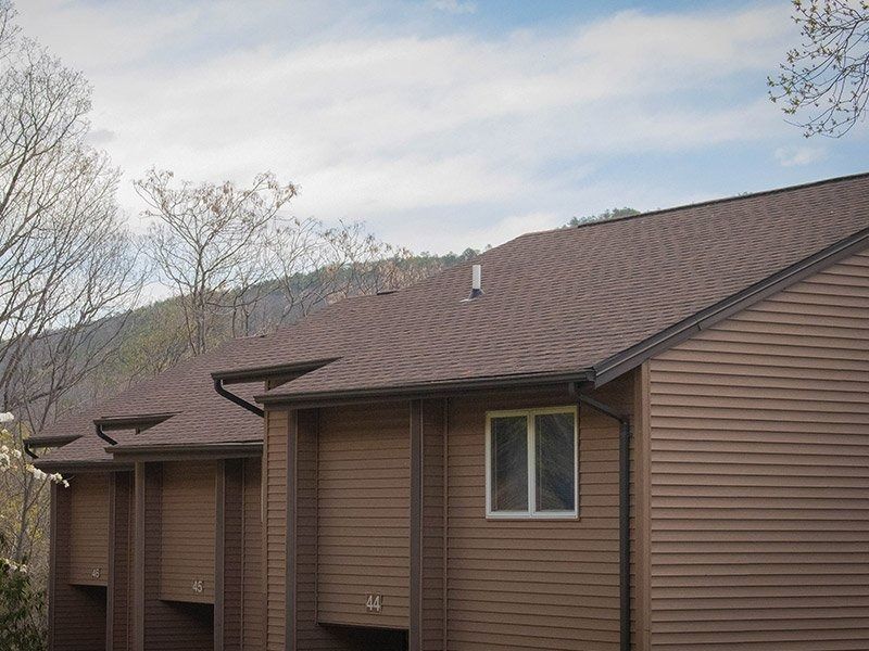 Brown-sided building with a brown roof against a mountain backdrop and cloudy sky.