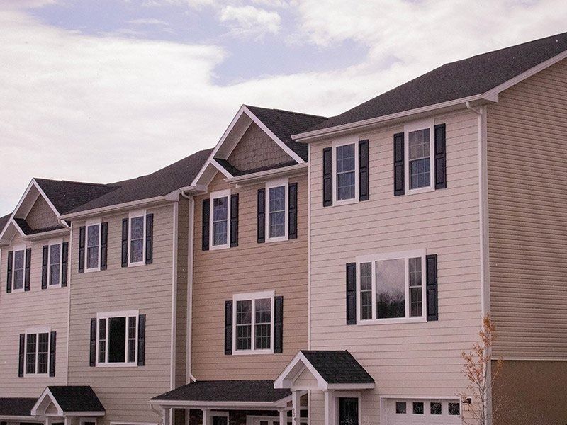 Row of townhouses with neutral siding, black shutters, and dark roofs.