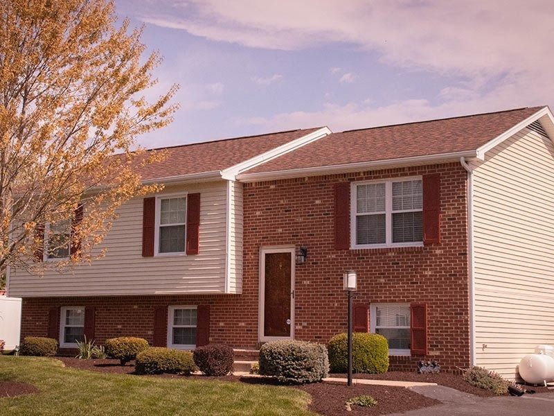 Split-level house with brick and beige siding, red shutters, lawn, and a tree with yellow leaves.