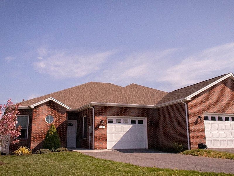 Red brick home with a two-car garage and a driveway under a blue sky.