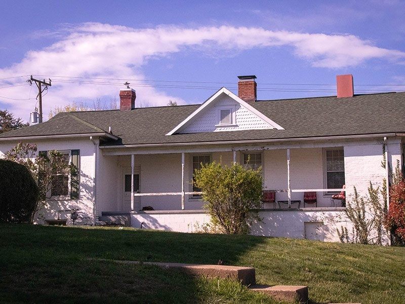 White house with green roof, porch, and red brick chimneys on a sunny day.