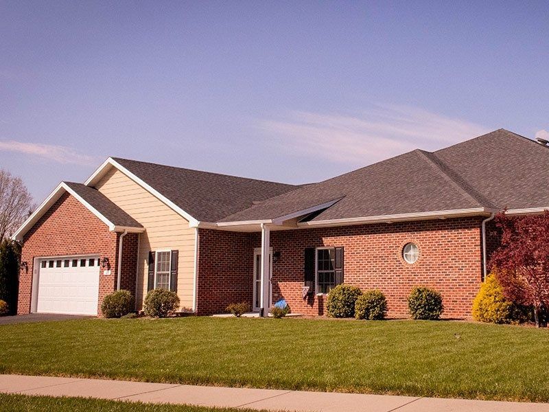 Brick ranch-style house with tan siding, green lawn, and blue sky.