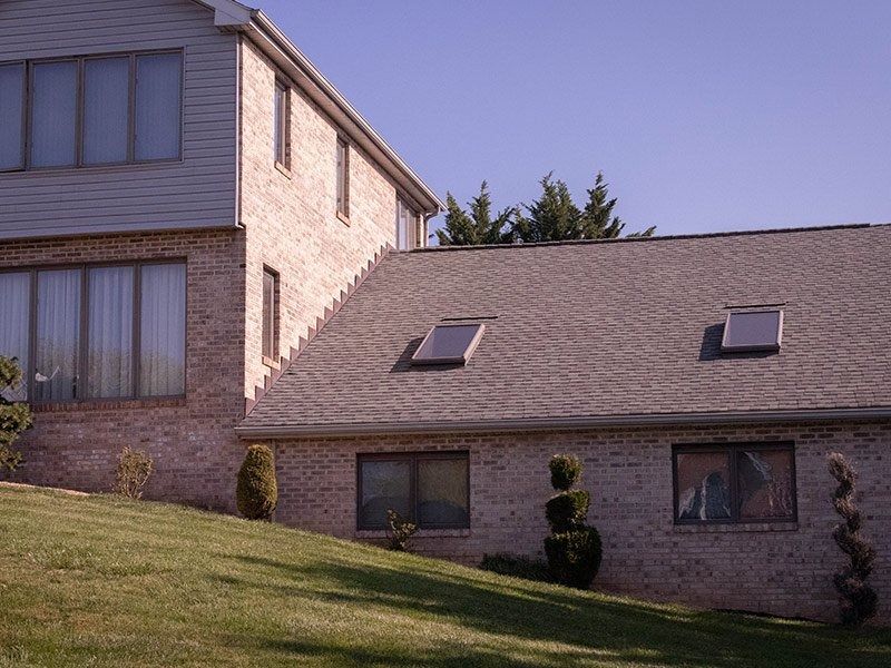 Two-story brick house with a sloped roof and skylights on a green grassy hill under a blue sky.