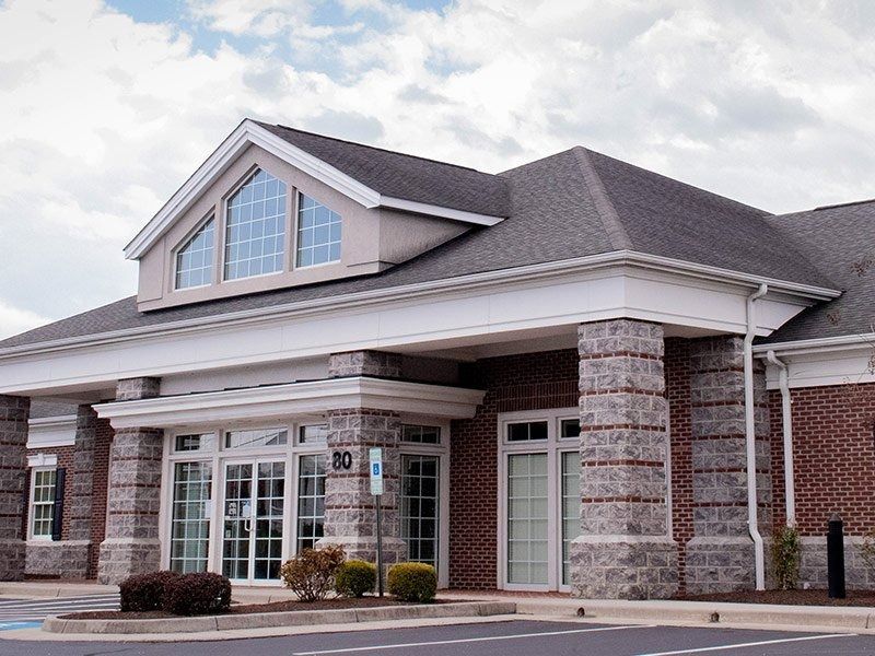 Brick building with gray roof, columns, and glass doors, likely a bank or office.