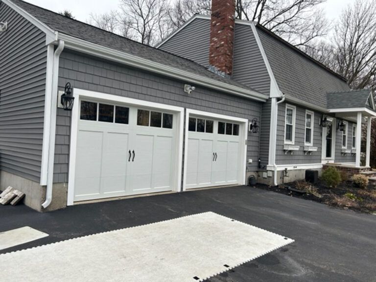 Gray house with white garage doors, black driveway, and dark shingles.