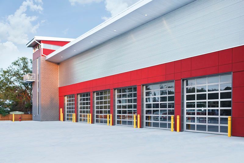 Fire station with red and silver facade, glass garage doors, and yellow bollards.