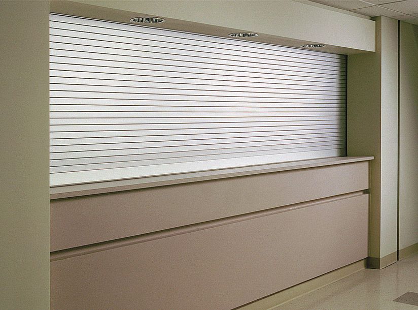 Reception desk with horizontal blinds in a beige room, and two horizontal drawers.
