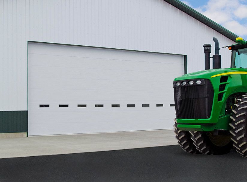 Green tractor next to a large white building with an open garage door.