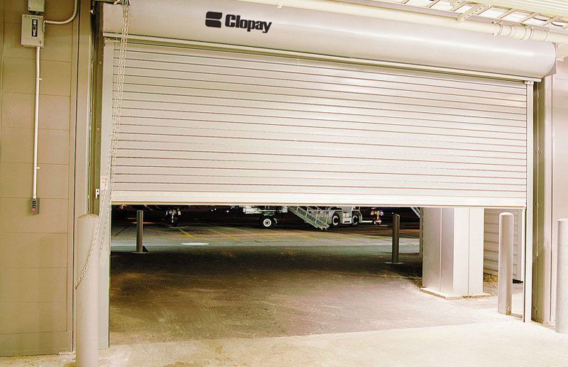 Rolling metal security gate partially open in an industrial setting.