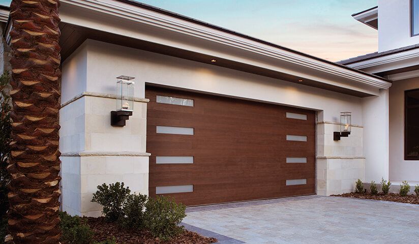 Brown garage door with horizontal glass panels, cream-colored house exterior, driveway, palm tree.