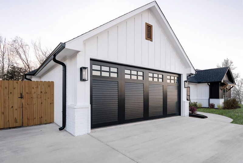 White house with black garage door, concrete driveway, and wooden fence.