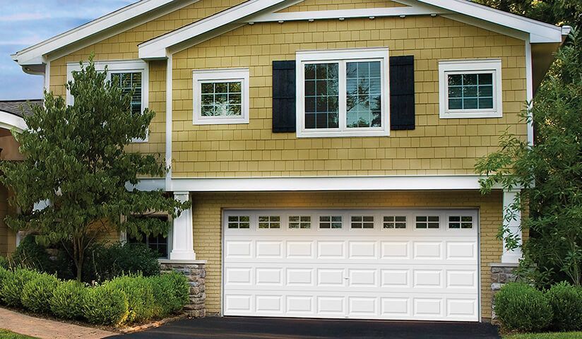 White garage door on a yellow house with windows and black shutters.