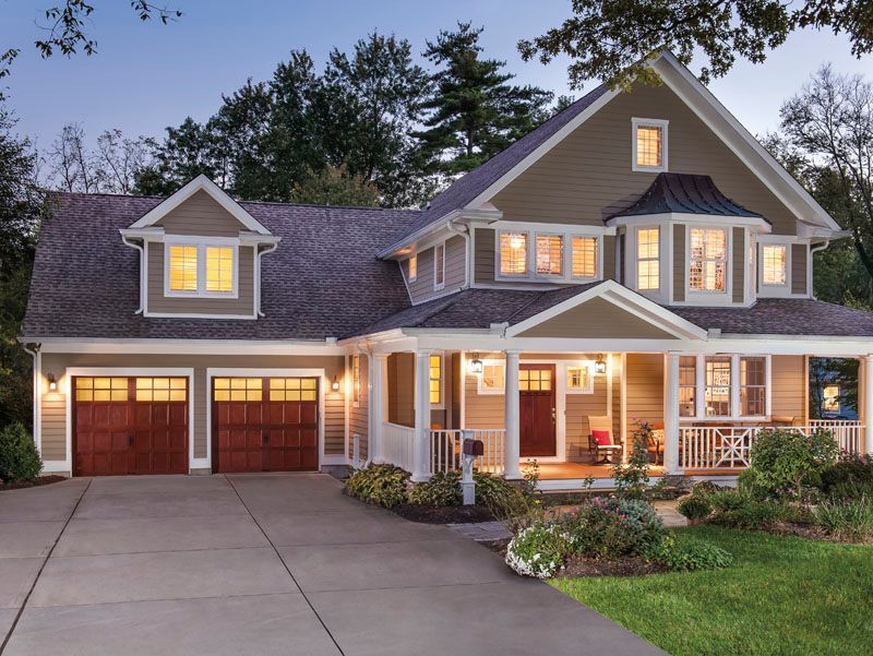 Two-story house with a brown exterior, porch, and a two-car garage. A driveway leads to the home, surrounded by landscaping.