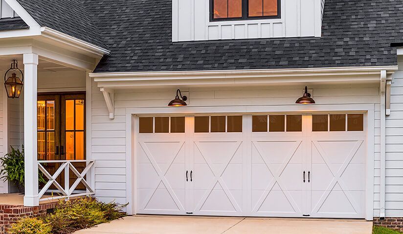 White garage door with diamond-shaped design, flanked by matching sconce lights, beside a white porch with a hanging lantern.