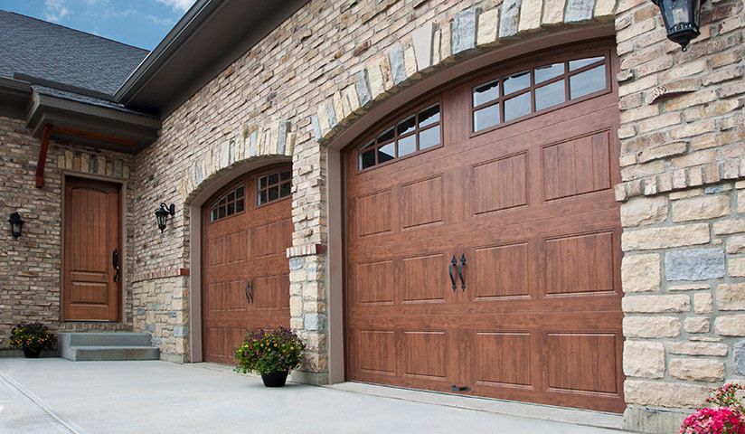 Stone facade with arched brown garage doors and a matching front door.