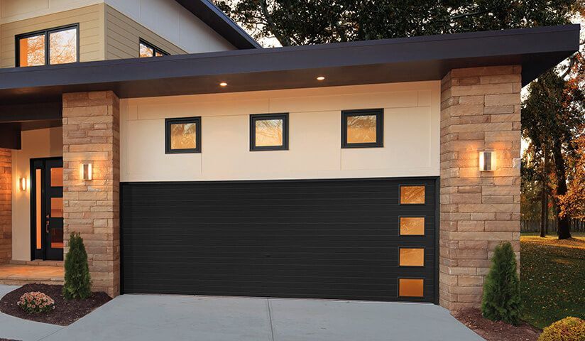 Modern home with black garage door, stone columns, and amber accent windows.