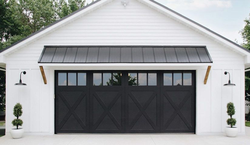 White garage with black door, awning, and outdoor lights. Two topiary trees flank the door.