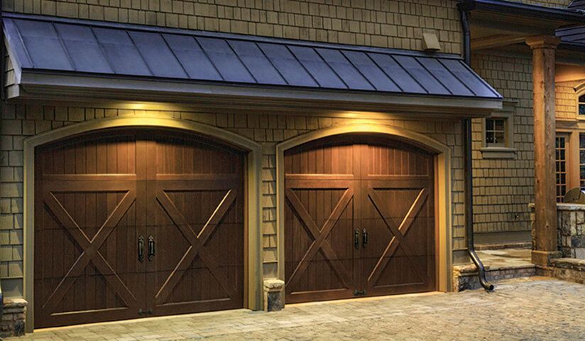 Wooden garage doors with arched tops and cross design, illuminated by warm lights.