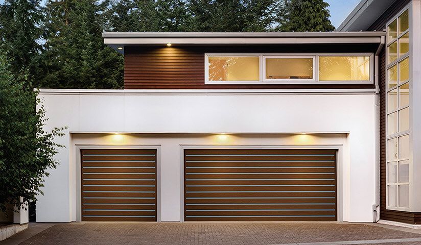 Two-car garage with brown horizontal slat doors, white walls, and a wood-paneled upper section with windows.