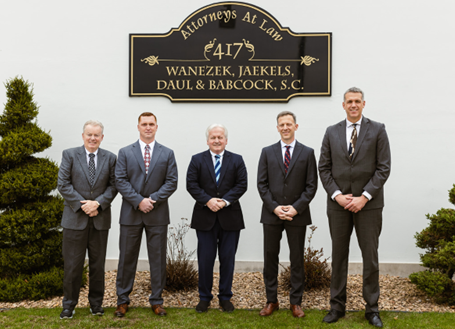 Five men in business suits stand side-by-side outdoors in front of a sign reading 