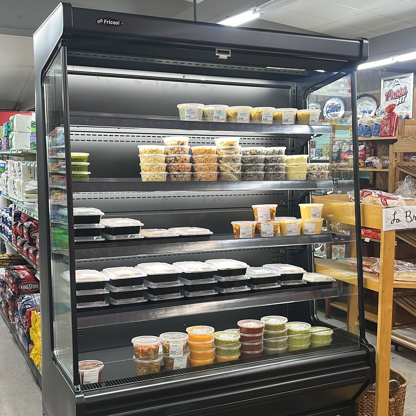 A black refrigerated display case in a grocery store filled with prepared foods in clear containers.