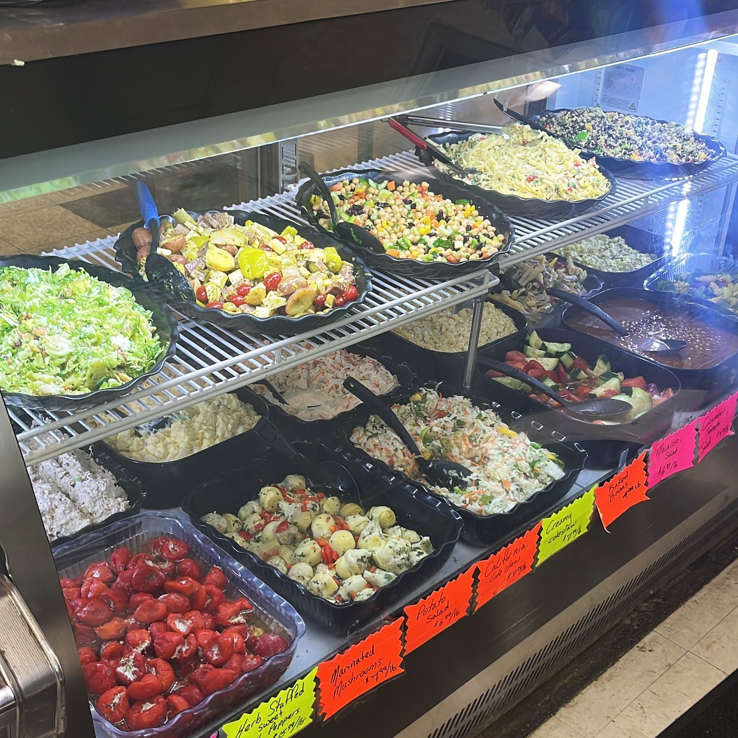 A display case with various salads in black trays.