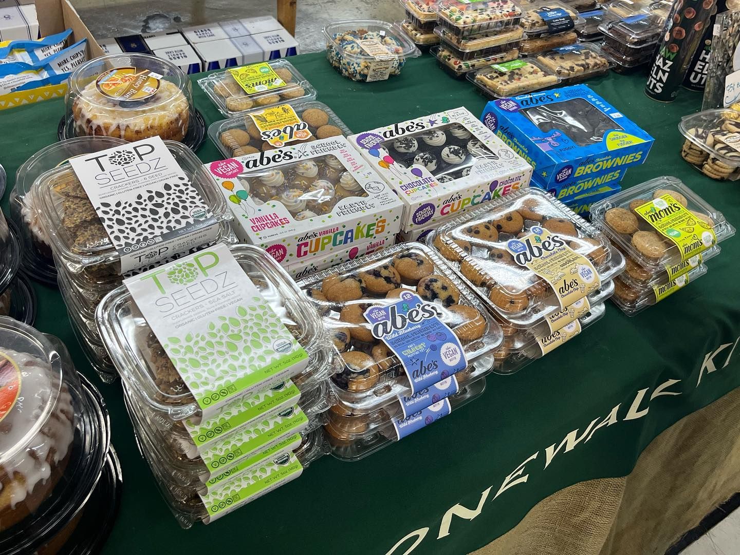 Bakery display: cakes, cookies, and pastries in clear plastic containers on a green table.