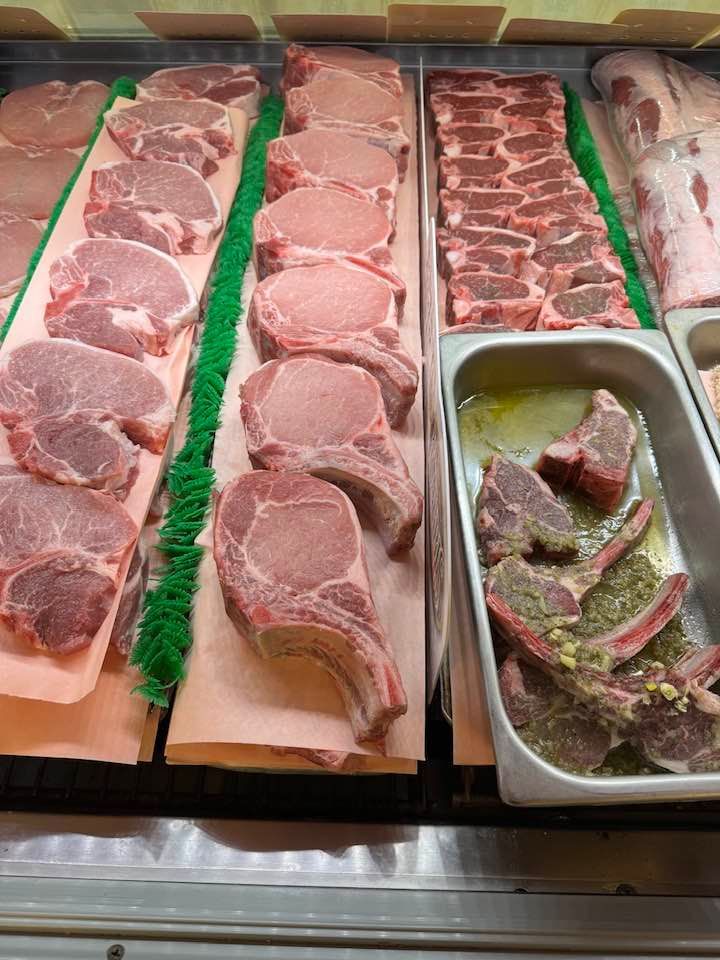 Display of various cuts of pork in a refrigerated deli case, including chops and ribs.