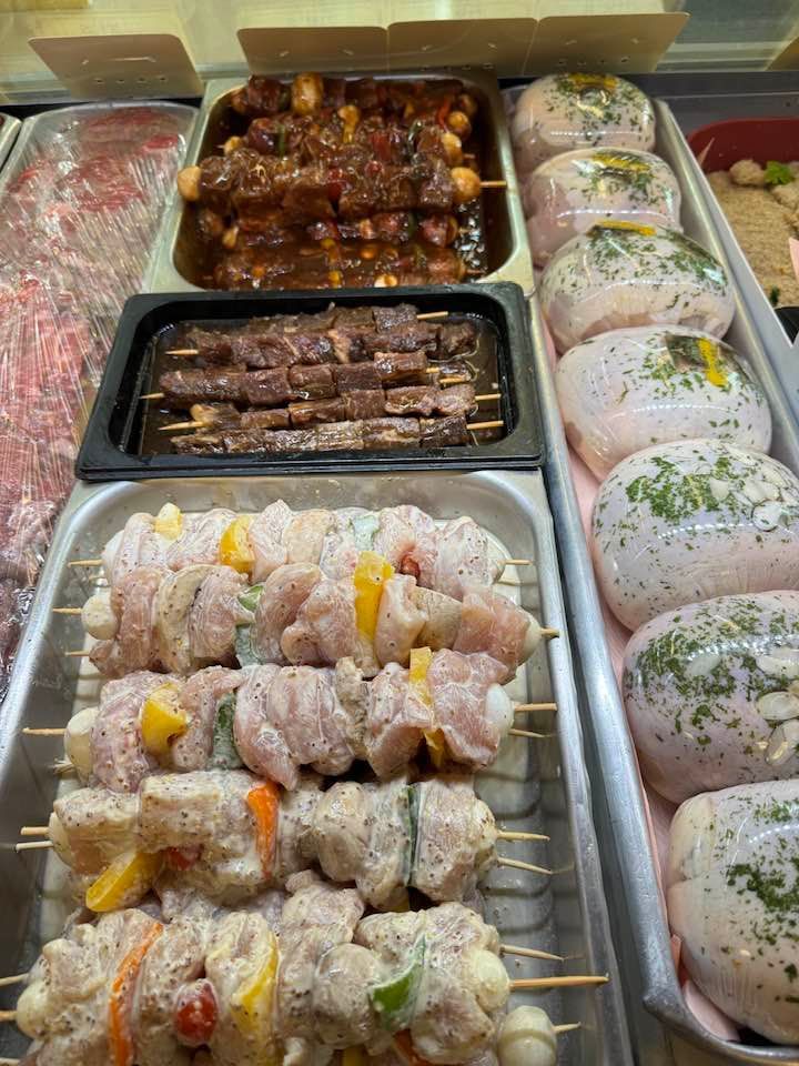 Display case with skewers of marinated meat and pre-made poultry rolls, ready for purchase.